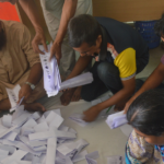People sitting on the ground, counting a pile of votes