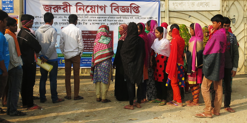 Would-be workers gather in front of the factory's main gate Would-be workers gather in front of the factory's main gate to read a banner advertising new job openings. © Elisa Oddone/Better Work Bangladesh
